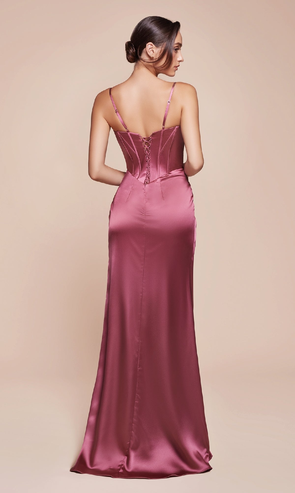Wearing the Ladivine 7495-1, a long satin prom dress with a slit, thin straps, and a lace-up back, a woman faces away from the camera.